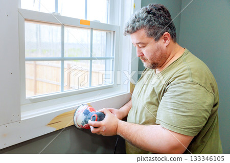 Contractor carefully applies putty to window frame, on his task during home renovation fresh paint new window. Contractor carefully applies putty to window frame, on his task during home renovation fresh paint new window. 133346105