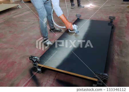 Paint worker uses spray gun to paint large wooden door with black paint Paint worker uses spray gun to paint large wooden door with black paint 133346112