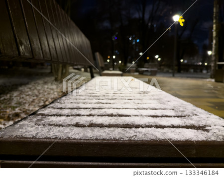 Close up photo of frozen bench in park at night. Snow completely covered the wooden bench in the city promenade. The park after the first snowfall, with frozen benches covered in snow Close up photo of frozen bench in park at night. Snow completely covered the wooden bench in the city promenade. The park after the first snowfall, with frozen benches covered in snow 133346184
