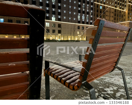 Frozen chair outside in the evening is covered in snow. A pedestrian area near a building with seats covered in snow. Cold weather with unpleasant sleet and frost 133346188