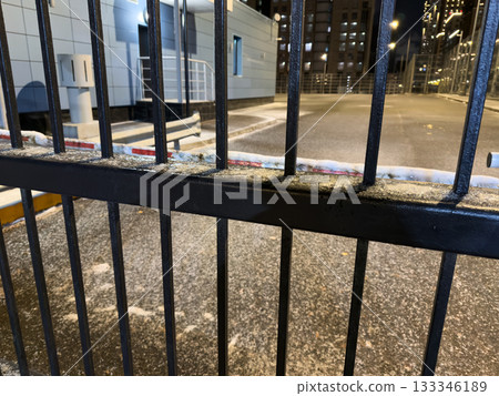 Closed off area for vehicles, secured by black metal gates and barrier, on cold, snowy evening. Snow covers the gate bars blocking entry to the secure area Closed off area for vehicles, secured by black metal gates and barrier, on cold, snowy evening. Snow covers the gate bars blocking entry to the secure area 133346189