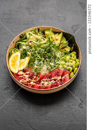 Colorful tuna poke bowl with rice avocado edamame and sesame on dark stone background Colorful tuna poke bowl with rice avocado edamame and sesame on dark stone background 133346372