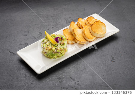 Avocado tartare with toasted baguette slices on white plate, gourmet appetizer 133346376
