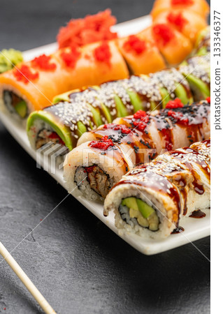 Assorted sushi rolls with salmon avocado and eel topped with sauces and sesame on plate Assorted sushi rolls with salmon avocado and eel topped with sauces and sesame on plate 133346377