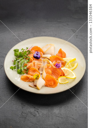 Assorted salmon sashimi with lemon, microgreens and edible flowers on plate 133346384
