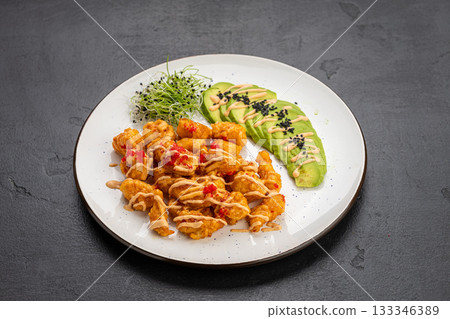 Crispy shrimp bites with spicy mayo, avocado slices and microgreens on a white plate 133346389