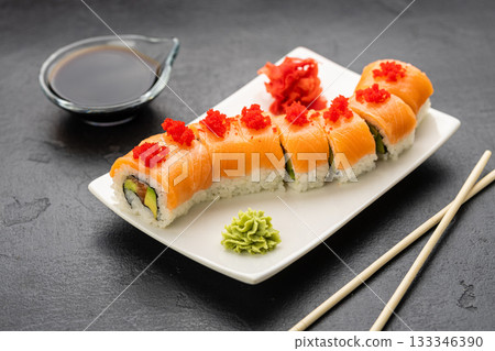 Salmon sushi roll with red roe on white plate, soy sauce, wasabi and ginger, top view Salmon sushi roll with red roe on white plate, soy sauce, wasabi and ginger, top view 133346390