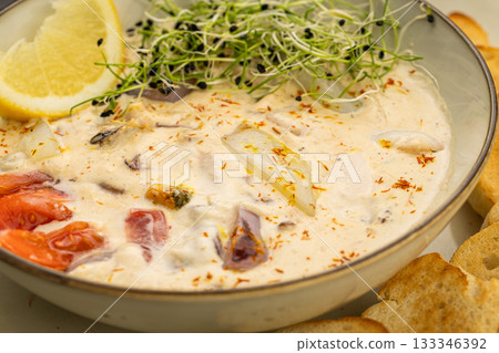 Creamy seafood chowder with lemon and microgreens, served with toasted baguette slices 133346392