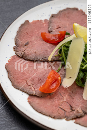 Beef carpaccio with arugula, parmesan shavings and lemon on a plate 133346393