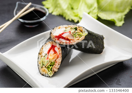 Sushi burrito halves with nori, crab, roe and veggies on white plate with soy sauce, close up 133346400