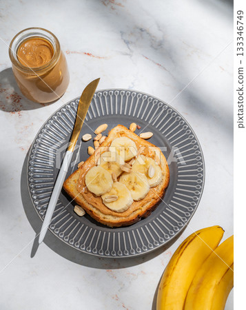 Peanut butter toast and banana on a dark plate on a marble background with fruits Peanut butter toast and banana on a dark plate on a marble background with fruits 133346749