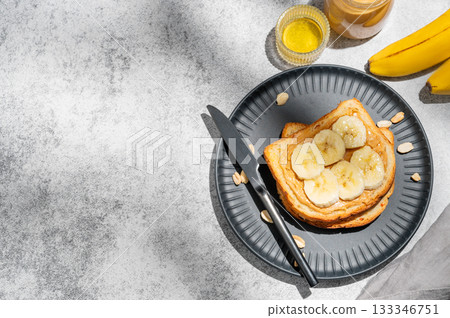 Peanut butter toast and banana on a black plate on a gray background with nuts 133346751