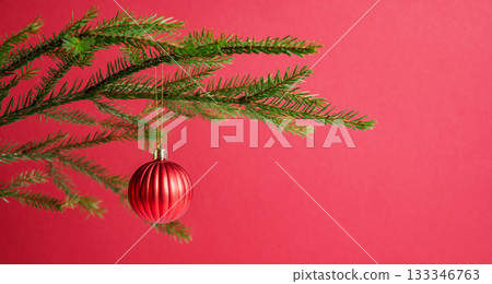 Fir branches with a ball-shaped Christmas tree ornament on a red background close up. 133346763