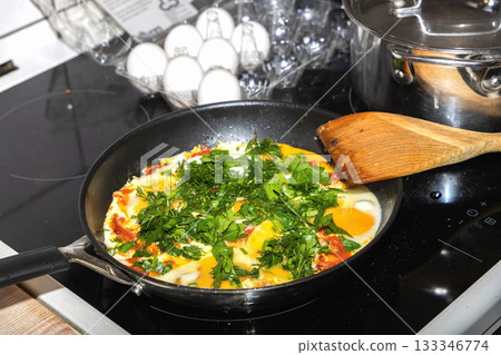 Fried eggs with tomatoes and herbs on induction stove 133346774