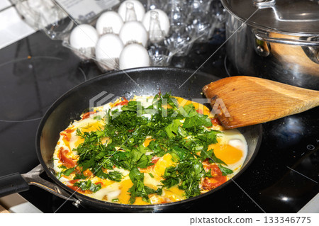 Homemade eggs with tomatoes and herbs cooking on induction stove 133346775