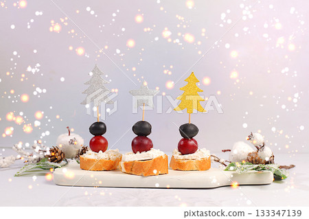 Christmas and New Year's dishes, a set of appetizers for the festive table. Canapes with soft mozzarella cheese, grapes, and olives on a marble table, Christmas Eve concept 133347139