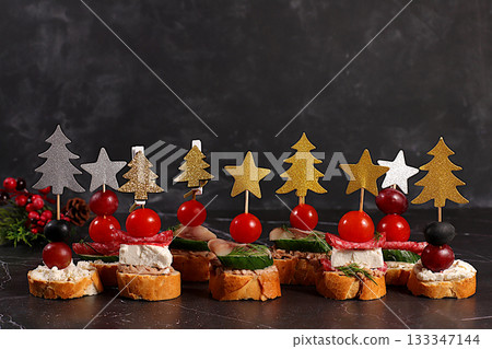 An assortment of various Canapes with tomatoes, pate, mozzarella cheese, salami, herring, olives, and grapes on a marble table. Christmas and New Year's dishes, a set of appetizers for festive table An assortment of various Canapes with tomatoes, pate, mozzarella cheese, salami, herring, olives, and grapes on a marble table. Christmas and New Year's dishes, a set of appetizers for festive table 133347144