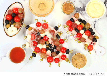 Christmas and New Year's dishes, a set of snacks and refreshing drinks for the festive table. A plate with canapes of tomatoes, mozzarella cheese, olives, black olives and grapes on a marble table Christmas and New Year's dishes, a set of snacks and refreshing drinks for the festive table. A plate with canapes of tomatoes, mozzarella cheese, olives, black olives and grapes on a marble table 133347156
