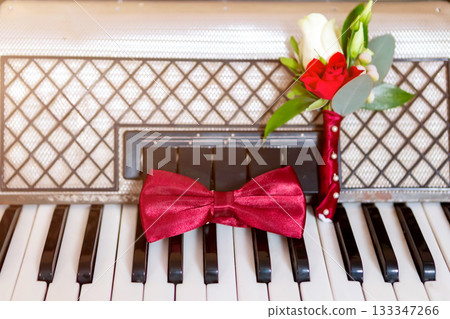 Red Bow Tie and Boutonniere on a Vintage Piano Keyboard in Soft Light. Red Bow Tie and Boutonniere on a Vintage Piano Keyboard in Soft Light. 133347266