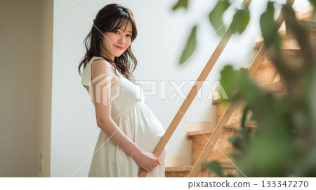 A natural photo of a pregnant woman in a white dress seen through a houseplant 133347270