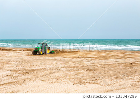 Spain, Valencia, March 29, 2024: Tractor Leveling Sand on a Beach by the Ocean on a Clear Day 133347289
