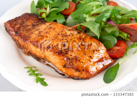 Grilled salmon fillet with fresh green salad and cherry tomatoes on a white plate. Keto diet. Grilled salmon fillet with fresh green salad and cherry tomatoes on a white plate. Keto diet. 133347385