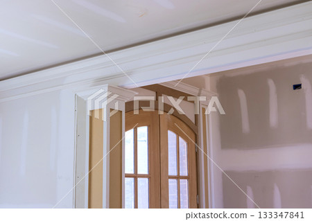 Workers are updating an interior doorway, adding trim while walls are being prepared for painting. 133347841