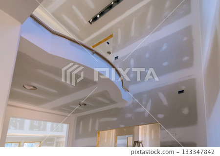 Workers prepare drywall in spacious home featuring stunning curved staircase for final painting Workers prepare drywall in spacious home featuring stunning curved staircase for final painting 133347842