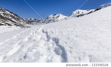 Snow-covered mountain landscape with recent footprints in pristine snow at Leirvassbu, Jotunheimen, Norway under a bright blue sky Snow-covered mountain landscape with recent footprints in pristine snow at Leirvassbu, Jotunheimen, Norway under a bright blue sky 133348326