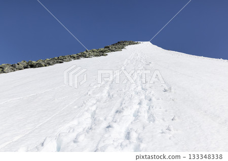 Snow-covered mountain landscape with footprints leading to a prominent peak in Leirdalen, Jotunheimen, Norway 133348338
