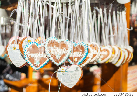 A row of small gingerbread hearts hangs neatly from white ribbons at a market stall. The soft sunlight highlights the icing borders and delicate handwritten patterns 133348533