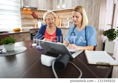 Compassionate nurse assists elderly woman with health concerns in cozy kitchen 133348920