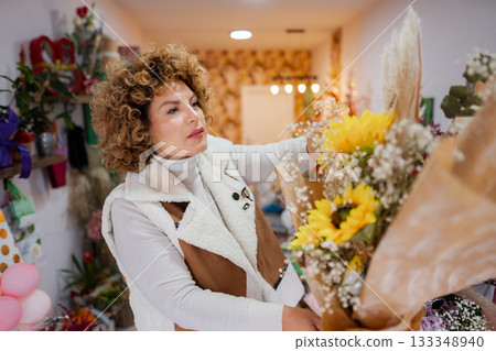 Woman arranging fresh flowers in a cozy flower shop during a bright afternoon 133348940