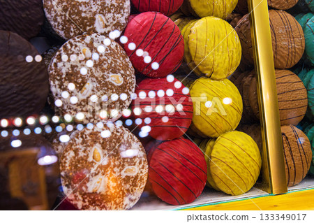 Assortment of vibrant hand-decorated gingerbread rounds in multiple colors and textures, arranged behind a glass counter with festive light reflections. Selective focus. 133349017
