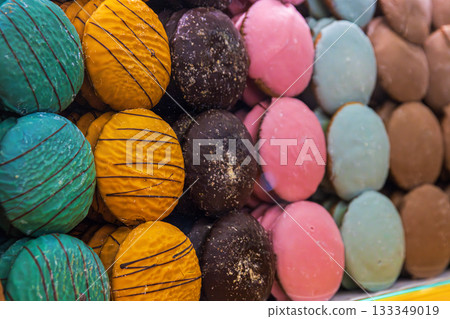 Assortment of vibrant hand-decorated gingerbread rounds in multiple colors and textures, arranged behind a glass counter with festive light reflections. Selective focus Assortment of vibrant hand-decorated gingerbread rounds in multiple colors and textures, arranged behind a glass counter with festive light reflections. Selective focus 133349019