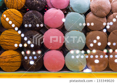 Assortment of vibrant hand-decorated gingerbread rounds in multiple colors and textures, arranged behind a glass counter with festive light reflections. Selective focus Assortment of vibrant hand-decorated gingerbread rounds in multiple colors and textures, arranged behind a glass counter with festive light reflections. Selective focus 133349020