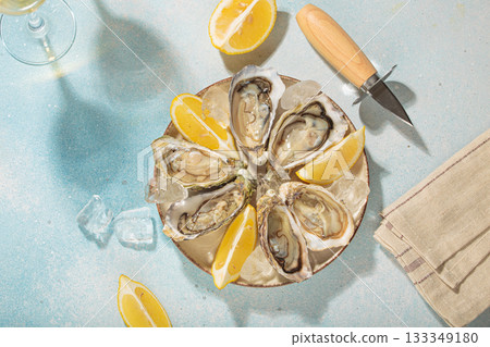Fresh oysters with lemon and white wine on ice for a luxurious meal on sunny day, blue background Fresh oysters with lemon and white wine on ice for a luxurious meal on sunny day, blue background 133349180