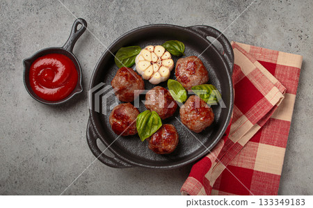Delicious fried meatballs with basil, garlic in cast iron pan and tomato sauce top view 133349183