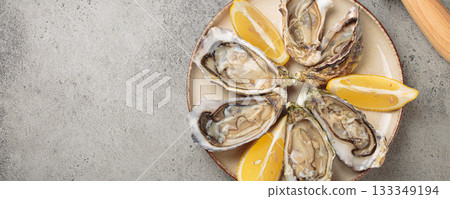 Fresh oysters with lemon wedges and oyster knife on plate top view, copy space 133349194