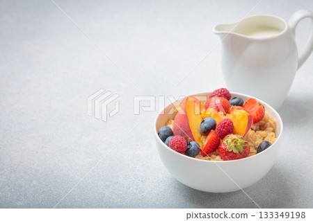 Oatmeal in bowl with peach, strawberry, raspberry, blueberry and milk for breakfast on white grey background, space for text 133349198