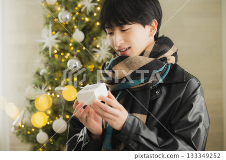 A man holding a present in front of a Christmas tree 133349252