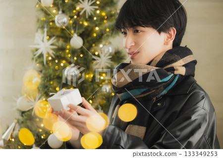 A man holding a present in front of a Christmas tree 133349253