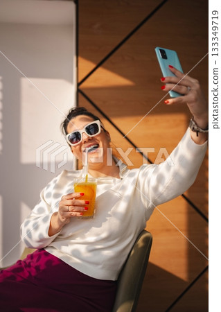 Joyful woman taking a selfie with a colorful drink in hand 133349719