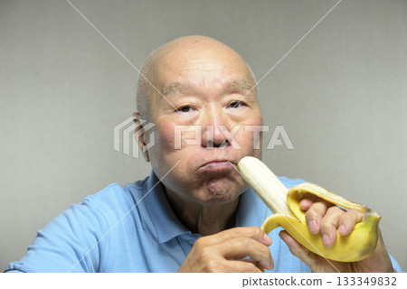 An elderly man eating a ripe banana with a smile 133349832