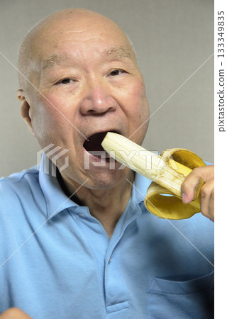An elderly man eating a ripe banana with a smile 133349835