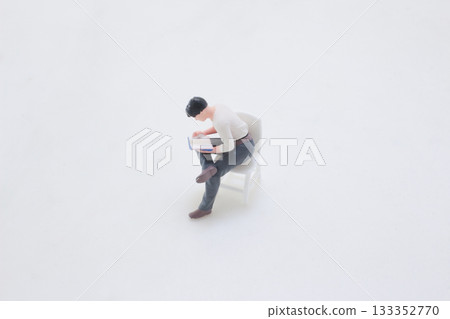Miniature Man Reading a Book While Seated on a White Chair Miniature Man Reading a Book While Seated on a White Chair 133352770