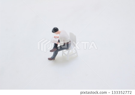 Miniature Man Reading a Book While Seated on a White Chair 133352772