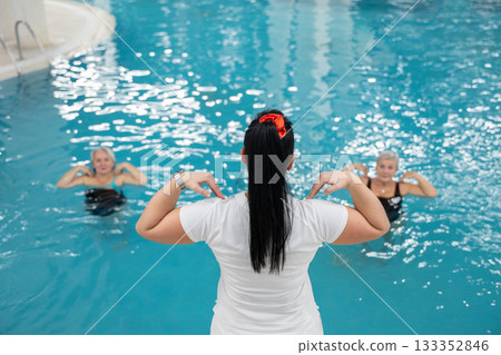 Instructor leading aquatic fitness training for group senior women in a swimming pool. Concept of health, exercise, wellness, water therapy, and active aging lifestyle Instructor leading aquatic fitness training for group senior women in a swimming pool. Concept of health, exercise, wellness, water therapy, and active aging lifestyle 133352846