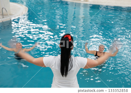 Instructor leading aquatic fitness training for group senior women in a swimming pool. Concept of health, exercise, wellness, water therapy, and active aging lifestyle 133352858