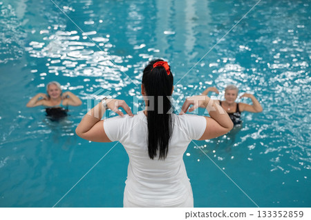 Instructor leading aquatic fitness training for group senior women in a swimming pool. Concept of health, exercise, wellness, water therapy, and active aging lifestyle 133352859
